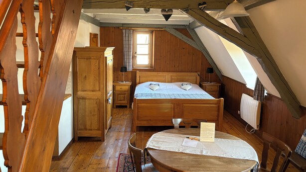 A cozy attic bedroom with a wooden bed, a small table, and a chair. - Duplex apartment with Alsatian decor (Beblenheim)