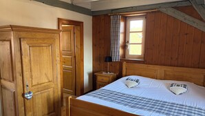A wooden bedroom with a bed, a wardrobe, a nightstand, and a window with curtains. - Duplex apartment with Alsatian decor (Beblenheim)