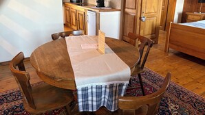 A cozy dining area with a round wooden table, chairs, and a checkered tablecloth. A kitchen with wooden cabinets and a microwave is visible in the background. - Duplex apartment with Alsatian decor (Beblenheim)