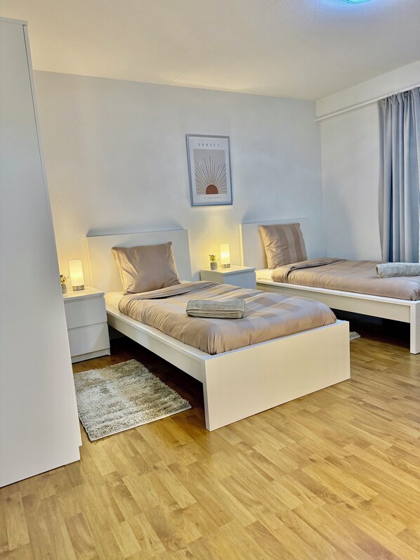 A modern bedroom with two beds, white nightstands, and a wall-mounted lamp.