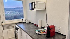 Ett kök med utsikt över staden, en mikrovågsugn, en brödrost, en vattenkokare, en tallrik med snacks och en röd kaffemaskin.