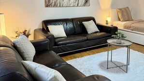 Ett modernt vardagsrum med en svart lädersoffa, en vit matta och ett litet, runt soffbord.