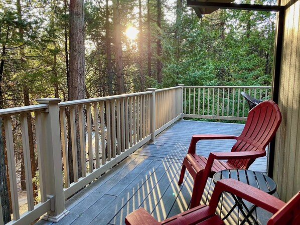 Une terrasse en bois avec une rambarde, deux chaises rouges et une table.