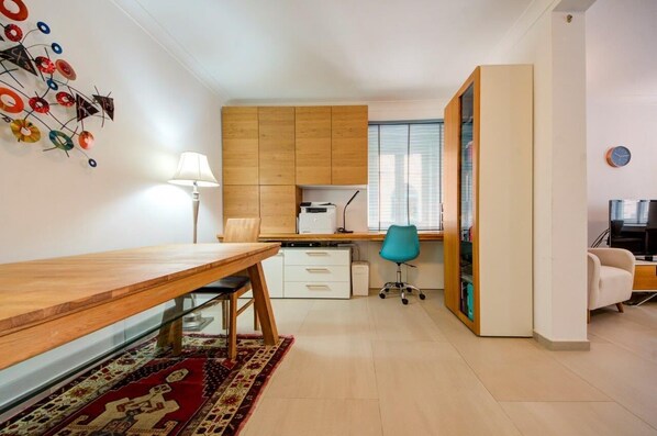 A modern apartment with a wooden dining table, a kitchen area, a blue office chair, and a large wardrobe.