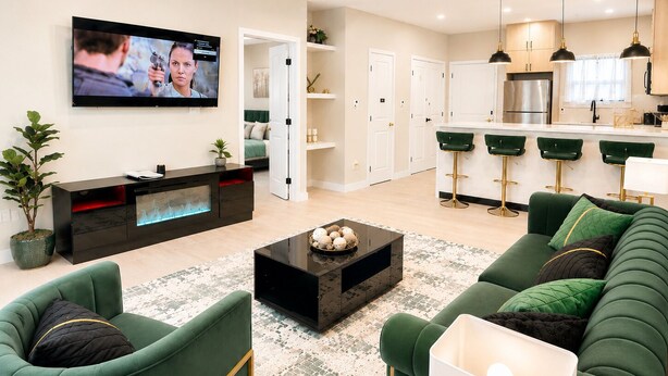Una sala de estar moderna con televisor, sofás verdes, una mesa de centro y una cocina con taburetes de bar.