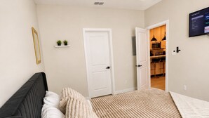 Un dormitorio con cama, ventilador de techo, televisor y puerta que da a una cocina.