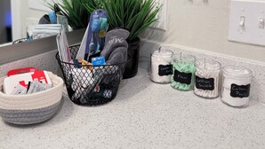 Un baño con lavamanos, dos espejos, una planta en maceta, toallero y una cesta con artículos de aseo.