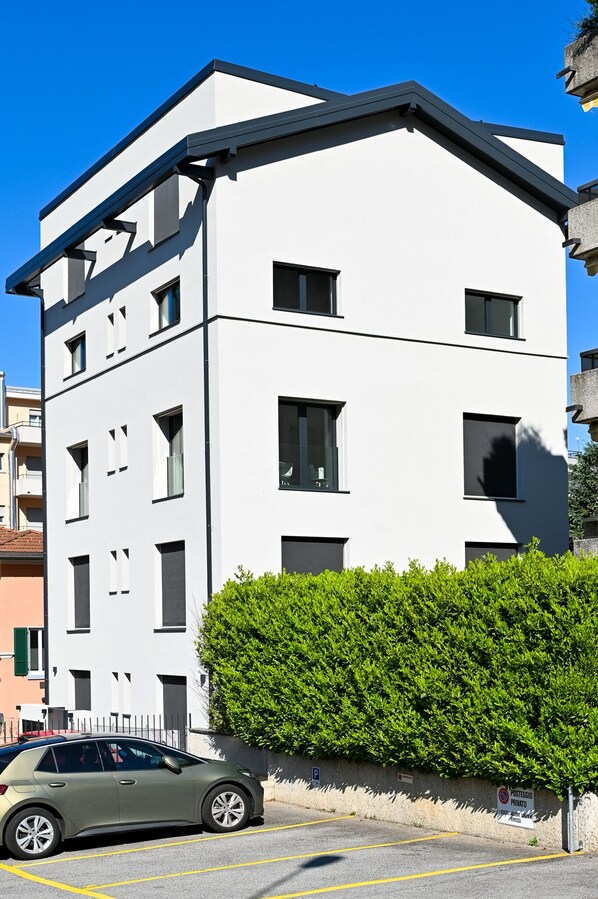 A modern multi-story building with a flat roof and a parking area in front. - Modern Concept Suite Crocetta 7 in Lugano (Lugano)