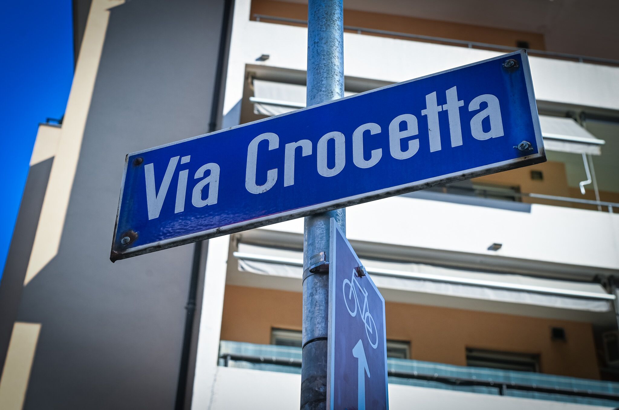 Ein Straßenschild mit der Aufschrift 'Via Crocetta', einem Fahrradsymbol und einem nach rechts zeigenden Pfeil.