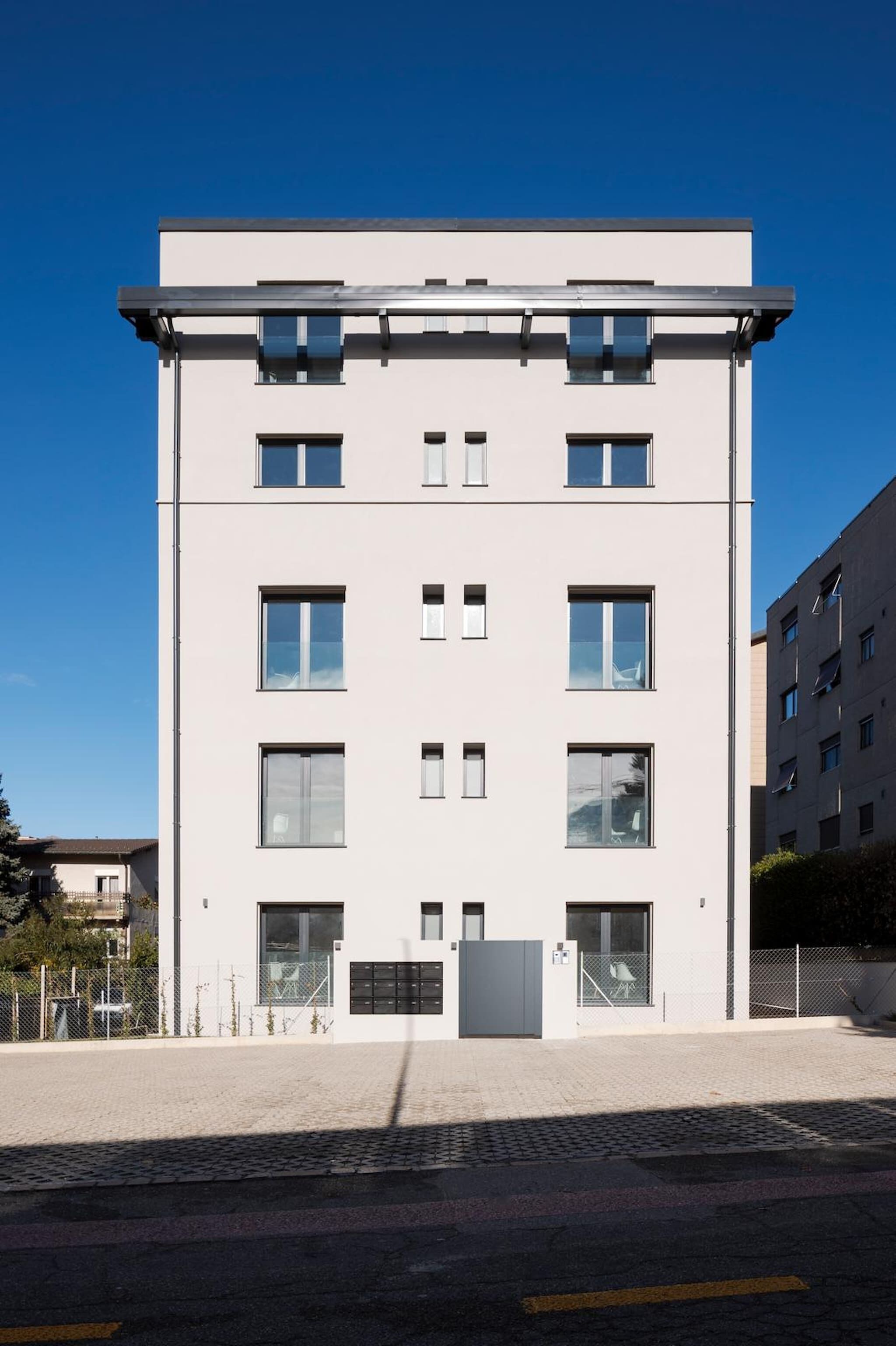 A modern building with a flat roof, multiple windows, and a gated entrance.