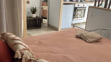 A bedroom with a bed, pillows, a bedside table, a mirror, and a view into a kitchen area.