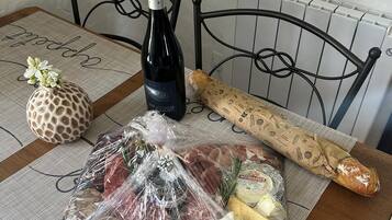 Une table avec une bouteille de vin, une baguette, un jambon emballé, du fromage et un objet décoratif.