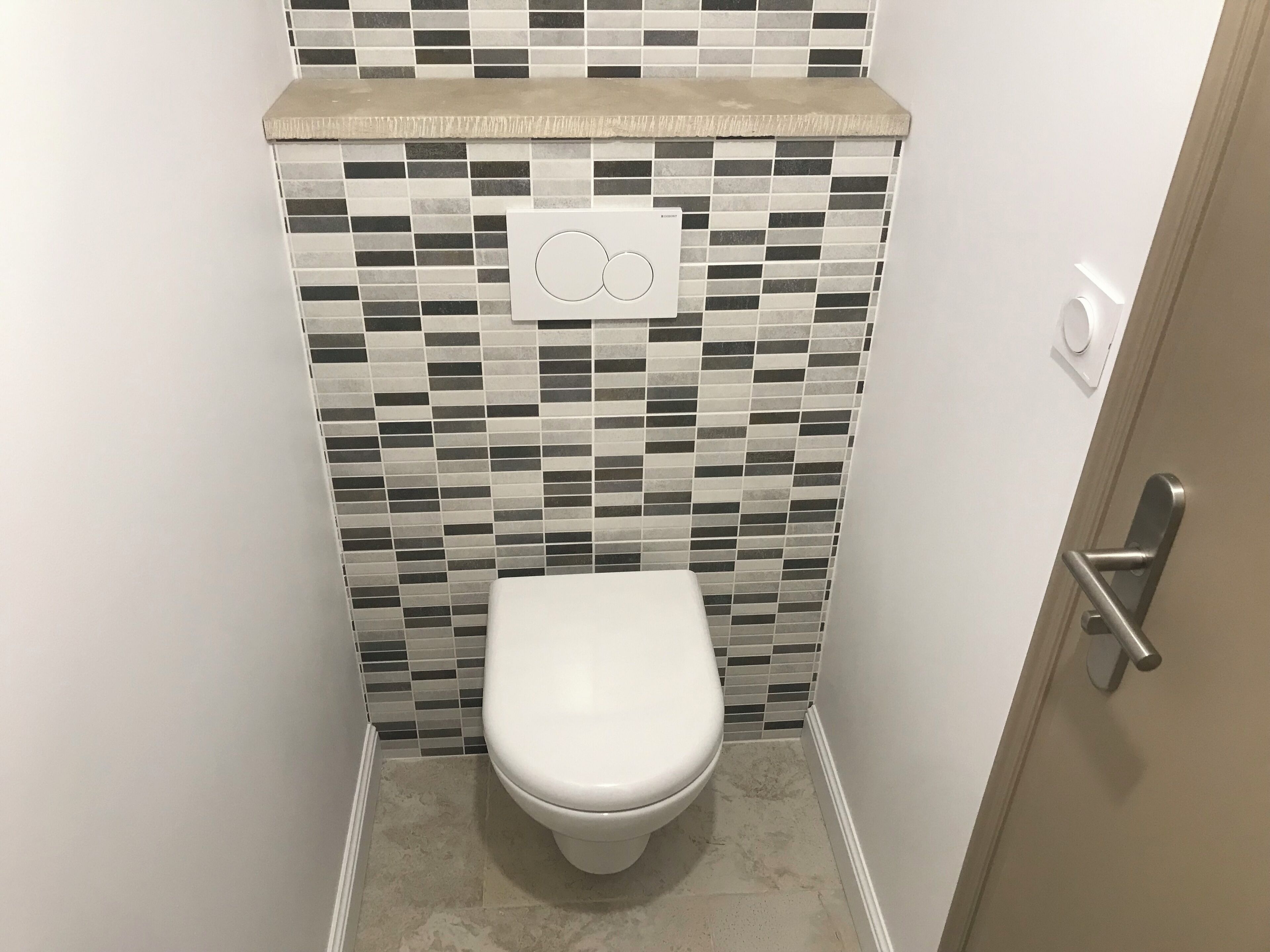 Een kleine, moderne badkamer met een betegelde spatwand en een wit toilet.