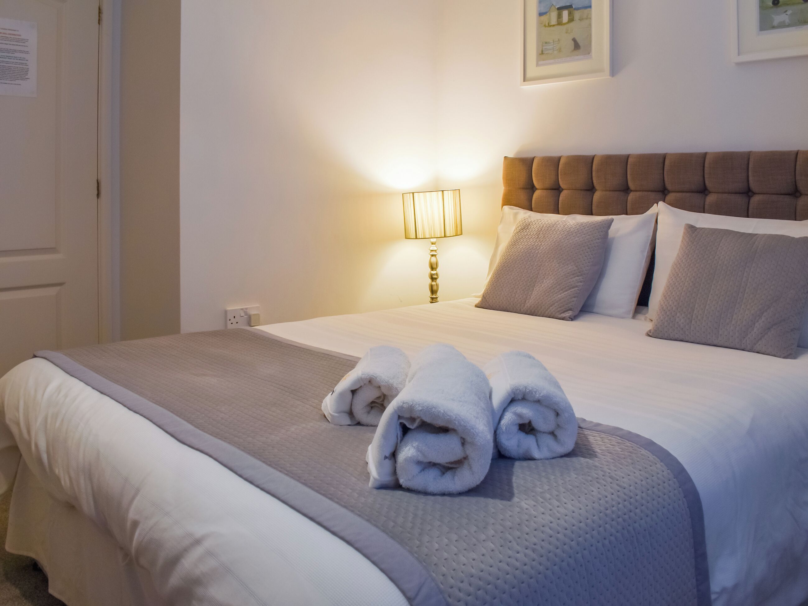 Una cama bien hecha con cabecera, una lámpara de noche y toallas enrolladas sobre la cama.