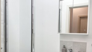 Un baño con cabina de ducha de vidrio, un lavabo con espejo y un cubo de basura.