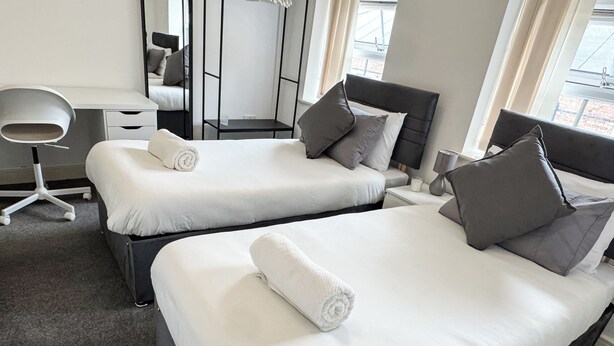 Una habitación de hotel con dos camas, un escritorio, una silla y un ventanal amplio.