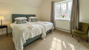 Quarto com cama, mesa de cabeceira, cadeira e janela com cortinas.