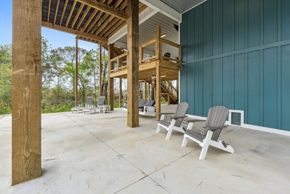 Un patio techado al aire libre con sillas Adirondack, una terraza de madera y vistas a los árboles circundantes.