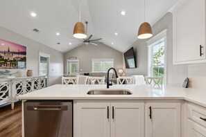 Una cocina moderna con una isla central, muebles blancos e iluminación colgante.