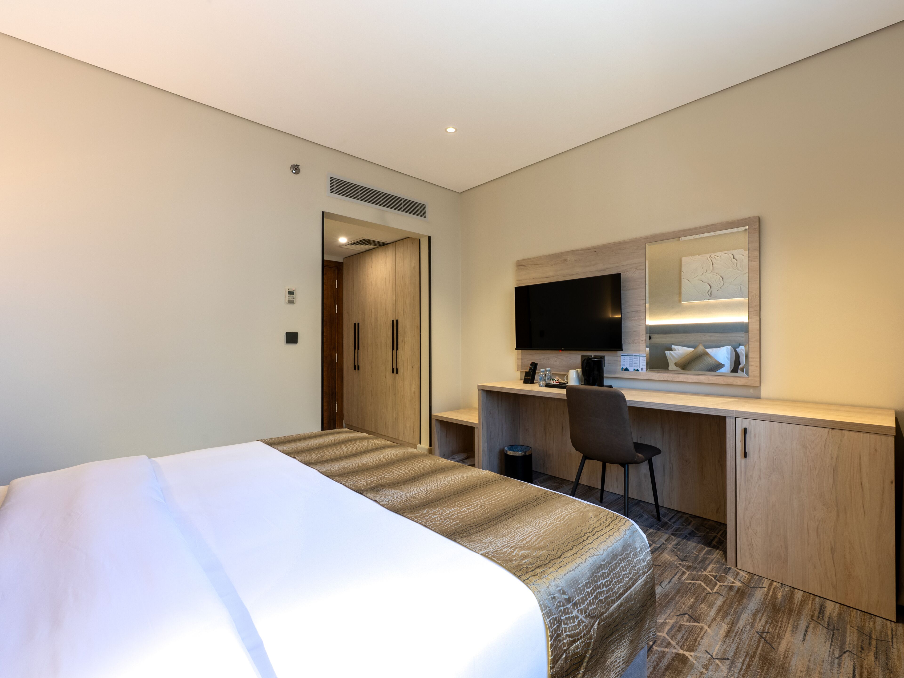 A hotel room with a bed, a desk, a chair, a television, and a mirror.