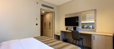 A hotel room with a bed, a desk, a chair, a television, and a mirror.
