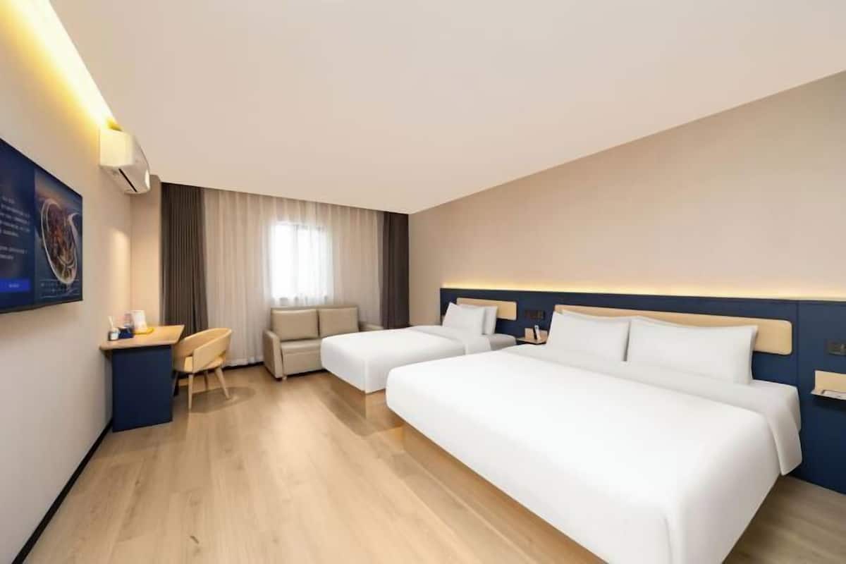Ein Hotelzimmer mit zwei Betten, einem Schreibtisch, einem Stuhl, einem Fenster mit Vorhängen und einer Wandklimaanlage.