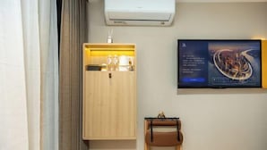 A hotel room with a wooden wardrobe, a mounted television displaying a cityscape, and a leather chair. - 7 Days Inn (Beijing South Railway Station Jiaomen West Subway Station Branch) (Beijing)