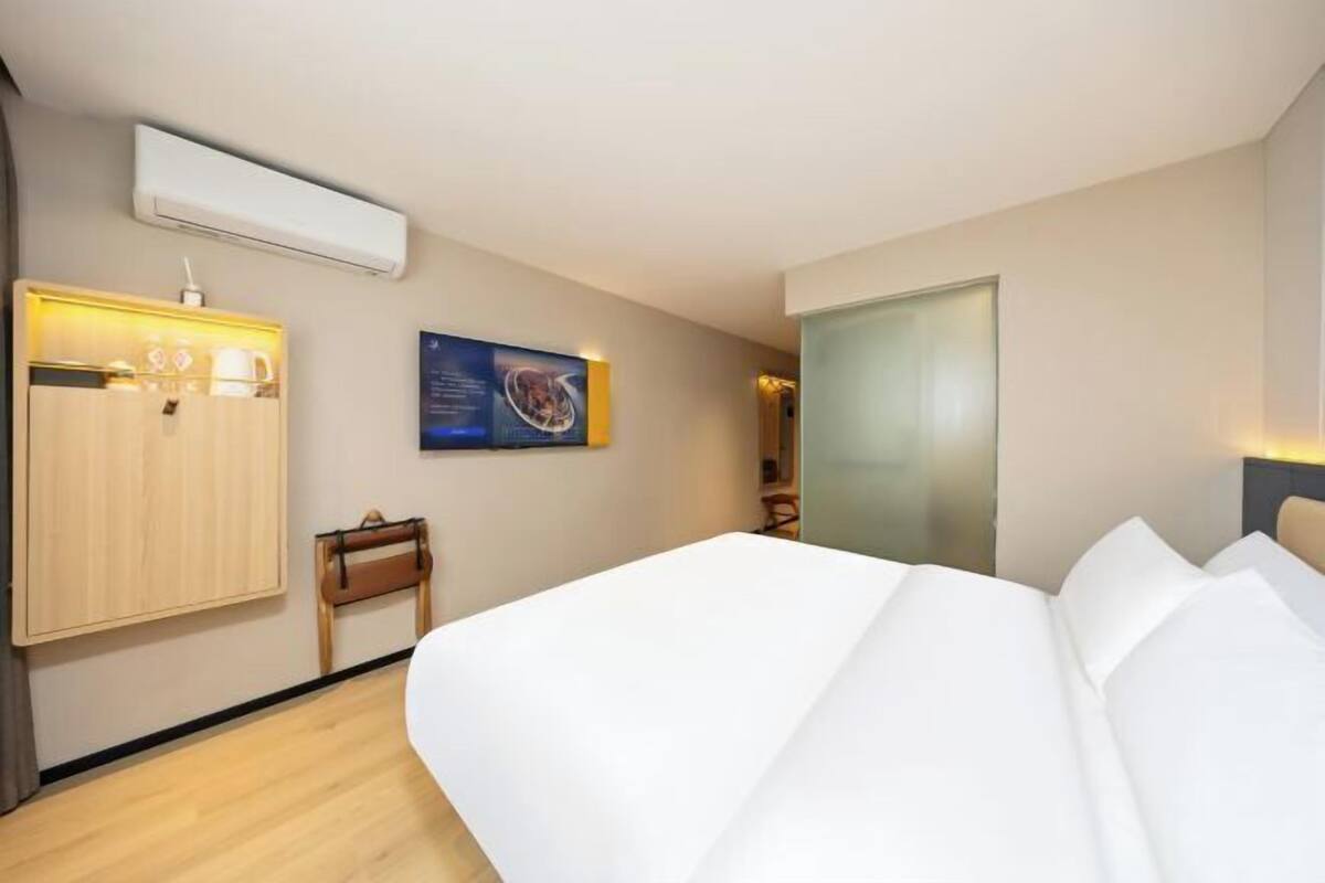 Ein Hotelzimmer mit einem Bett, einem Kleiderschrank, einem kleinen Tisch, einer Wand-Klimaanlage und einem gerahmten Bild.