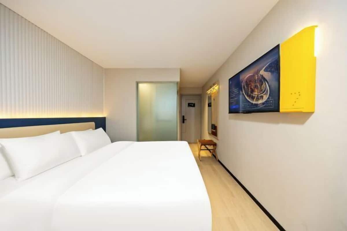 Ein Hotelzimmer mit einem Bett, einem Wandbild und einer Tür zu einem anderen Raum.