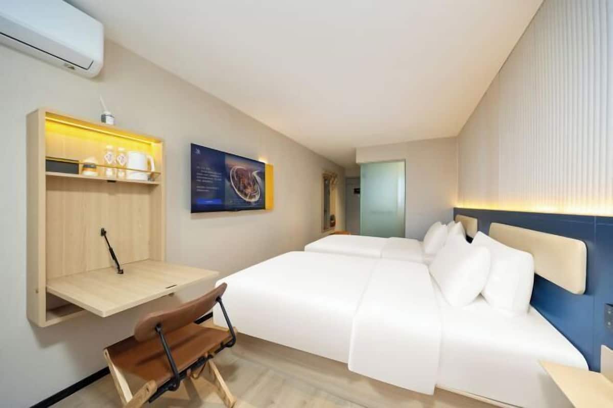 Ein Hotelzimmer mit einem Bett, einem Schreibtisch mit Stuhl, einem Wandregal mit Gegenständen und einem gerahmten Bild.