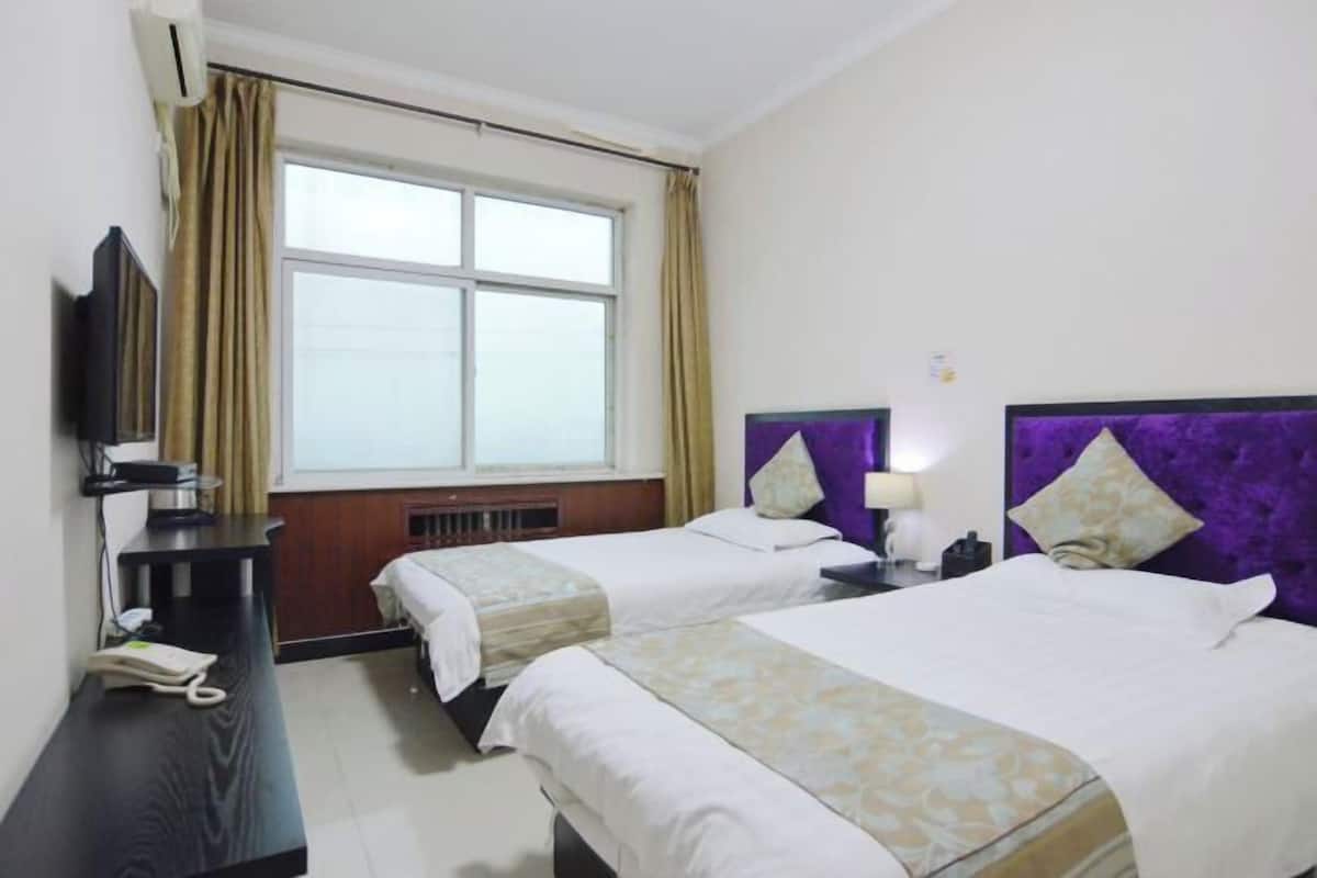 Une chambre d’hôtel avec deux lits, un bureau, une télévision et une fenêtre avec des rideaux.