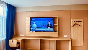A modern room with a flat-screen TV mounted on a wooden panel wall, a desk with a chair, and a wooden wardrobe with a hanger. - Fangxing Express Hotel (Shijiazhuang Luquan Zoo) (Shijiazhuang)