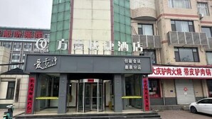 A hotel entrance with a revolving door, a signboard with Chinese characters, and a parked car. - Fangxing Express Hotel (Shijiazhuang Luquan Zoo) (Shijiazhuang)