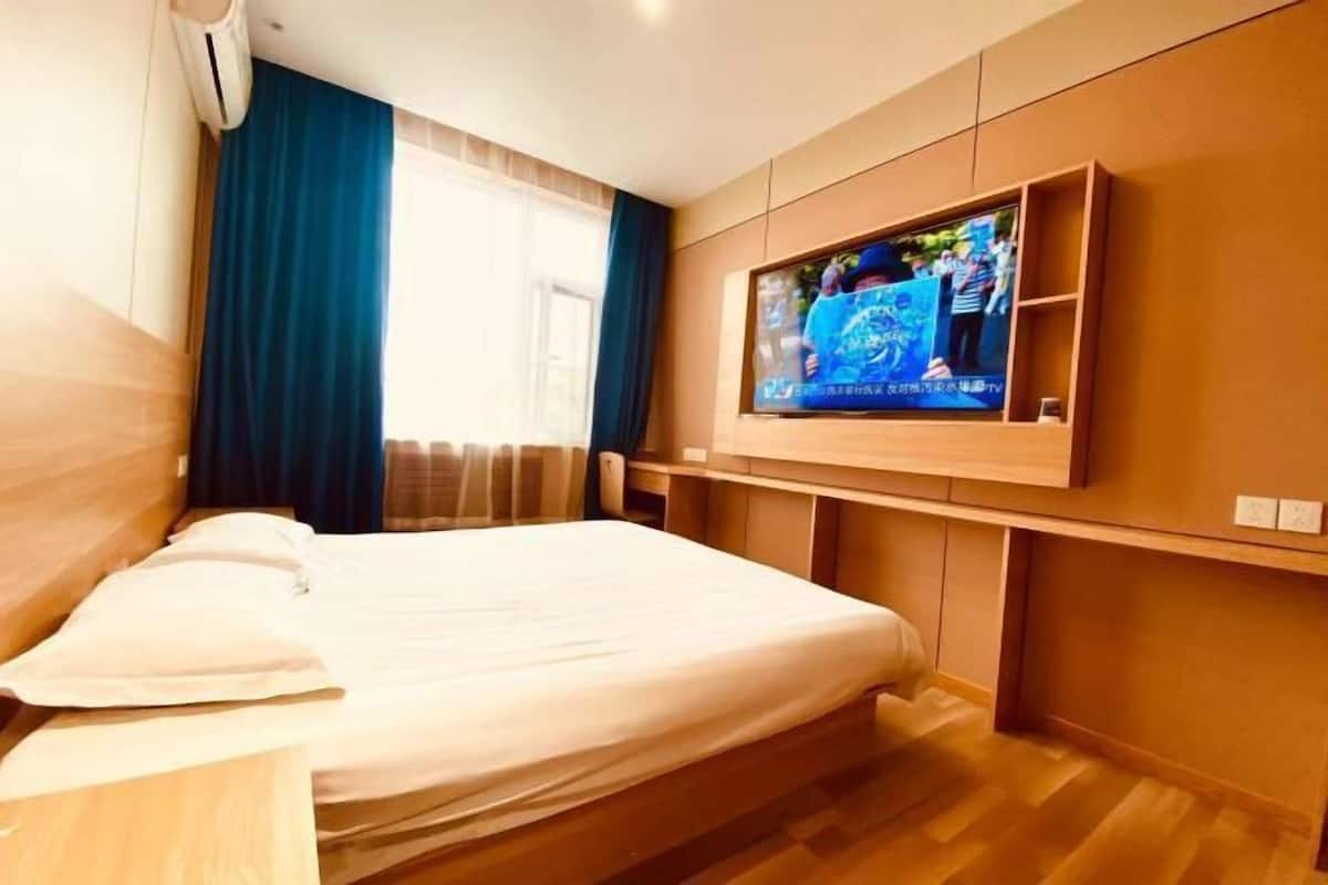 Une chambre d’hôtel avec un lit, un téléviseur fixé au mur et une fenêtre avec des rideaux.