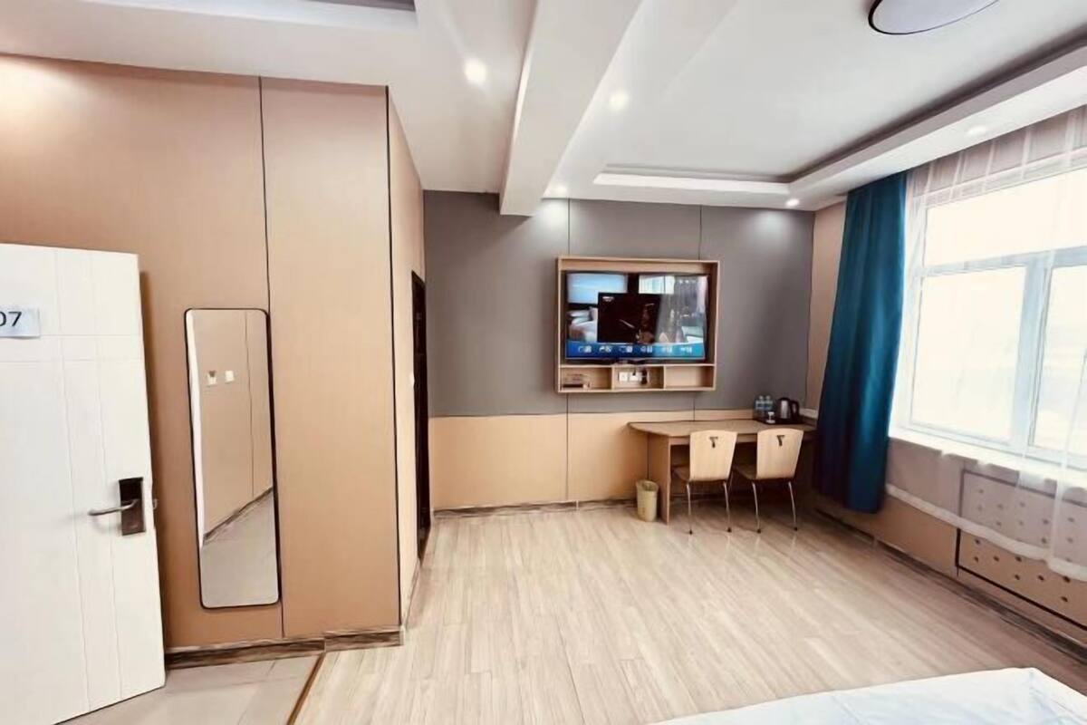 Une chambre d’hôtel équipée d’un lit, d’un bureau, d’une chaise, d’une armoire, d’une télévision et d’une fenêtre avec des rideaux.