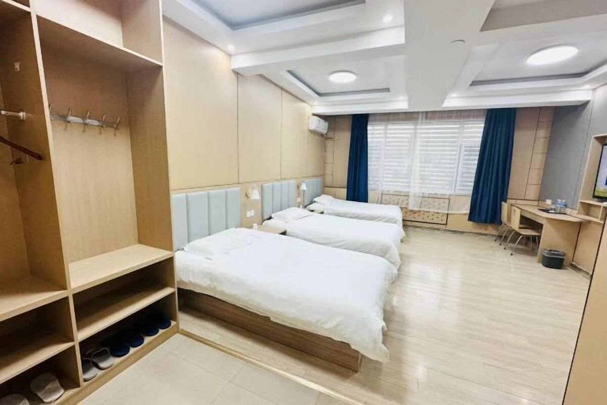 Une chambre d’hôtel avec trois lits, un bureau et une armoire avec un espace pour ranger les chaussures.