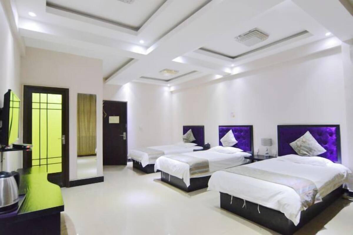 Une chambre d’hôtel avec trois lits, un téléviseur à écran plat, une machine à café et un miroir.