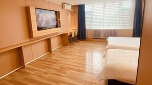 Habitación de hotel con piso de madera, un televisor en la pared, cama y ventana con cortinas.
