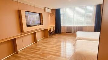 Ett hotellrum med trägolv, en tv som är monterad på väggen, en säng och ett fönster med gardiner.