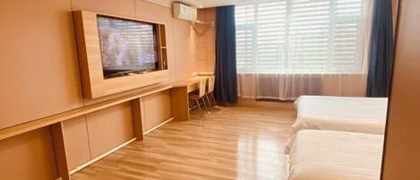 A hotel room with a wooden floor, a TV mounted on the wall, a bed, and a window with curtains.