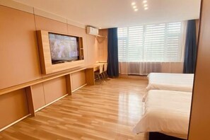 Habitación de hotel con piso de madera, un televisor en la pared, cama y ventana con cortinas.