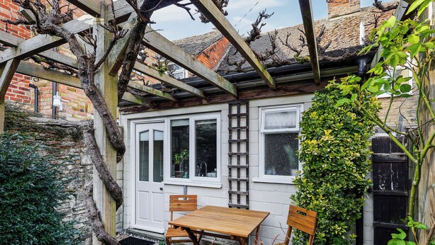 Un petit jardin clos, avec une table et des chaises en bois, une porte blanche et un mur en briques.