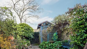 Un jardin avec un chemin de gravier menant à un bâtiment bleu doté d’un toit en pente et d’une nichoir sur le toit.