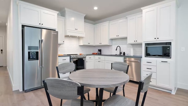 Een moderne keuken met witte kastjes, roestvrijstalen apparatuur en een ronde eettafel met stoelen.