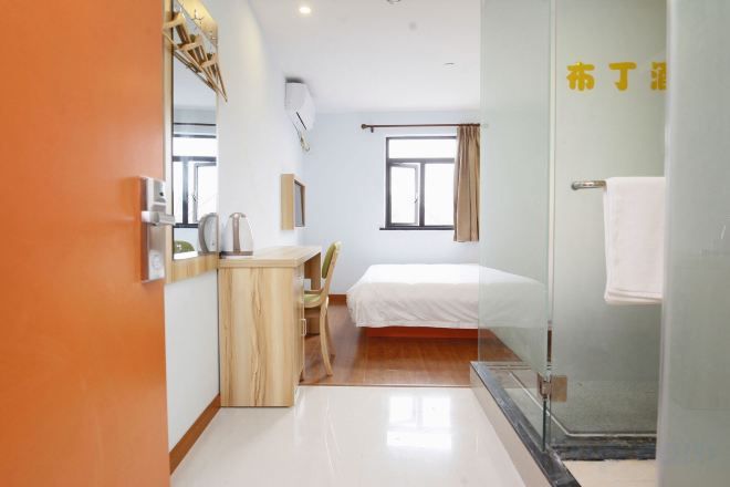 A hotel room with a bed, a desk, a chair, a glass shower enclosure, and a window.