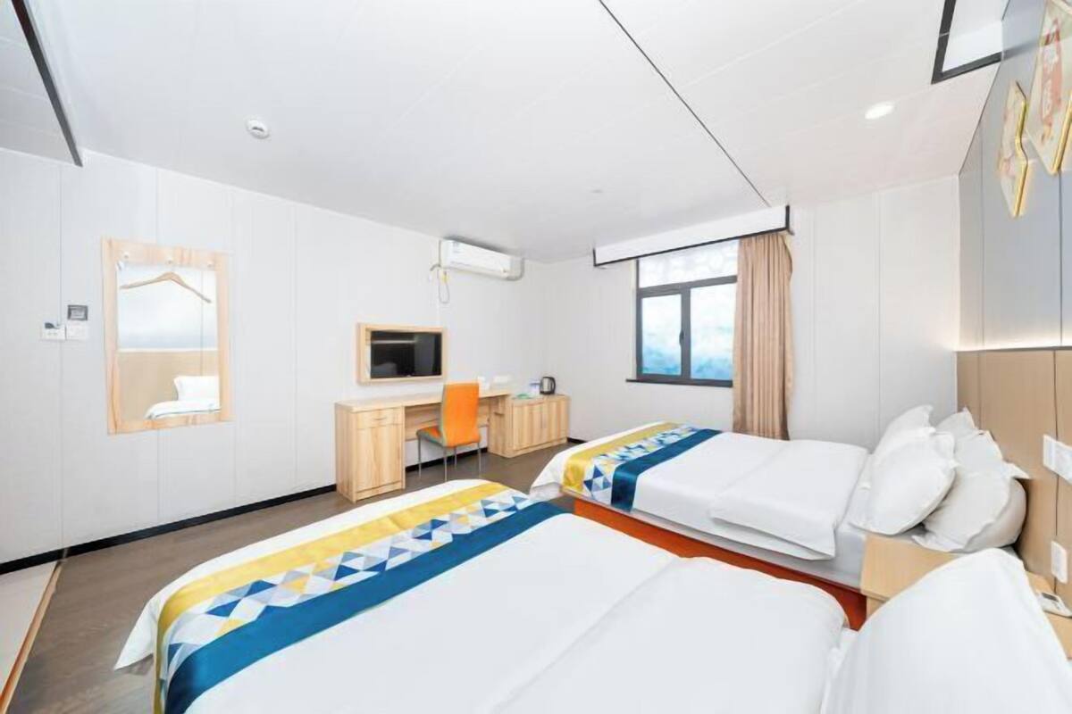 A hotel room with two beds, a desk, a chair, a TV, and a window.