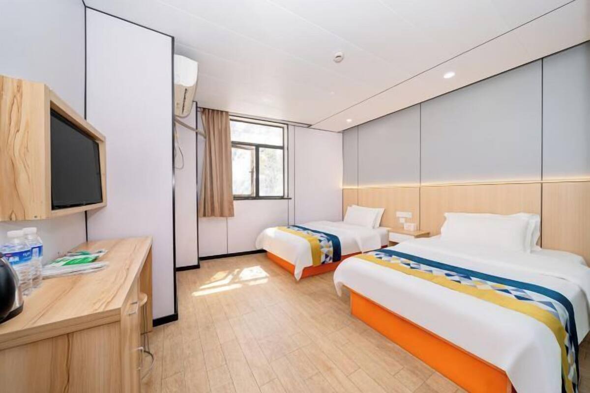 A hotel room with two beds, a desk with a chair, a television, and a window.