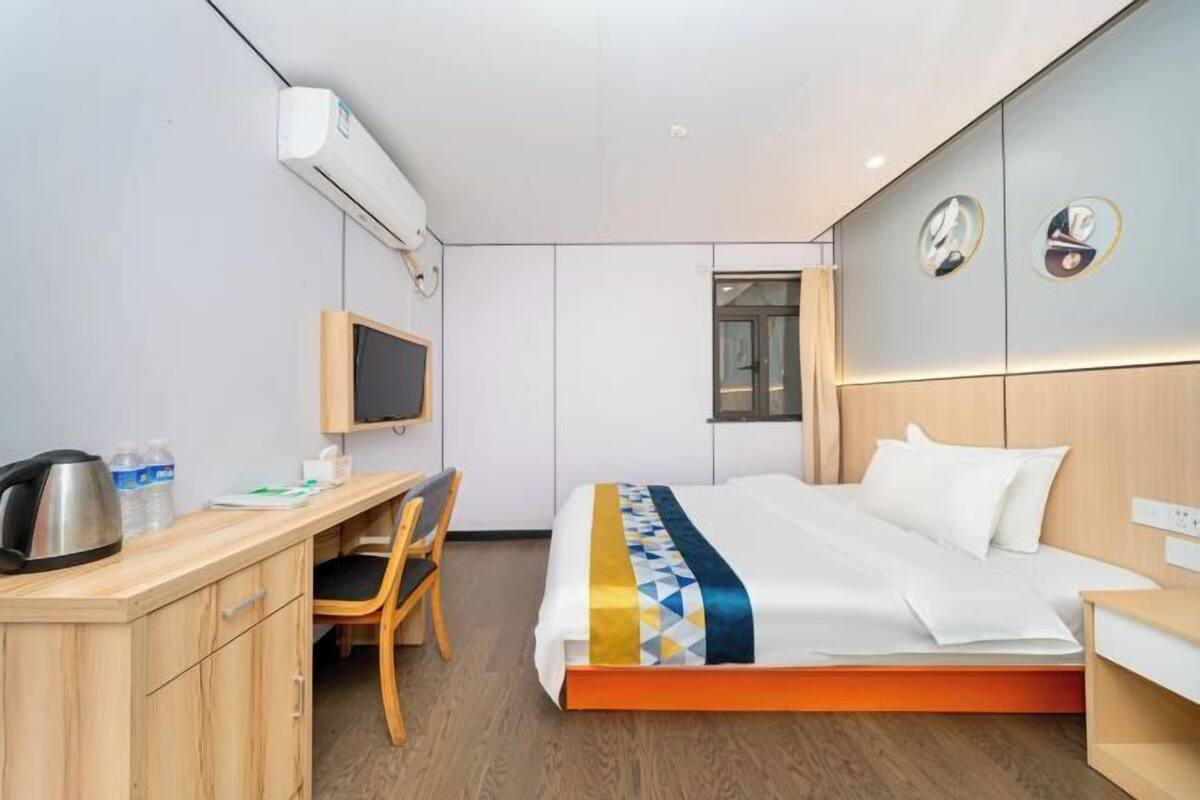 A hotel room with a bed, a desk, a chair, a television, and an air conditioning unit.