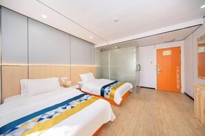 Et hotelværelse med to senge, en glasvæg, en orange dør og trægulv.