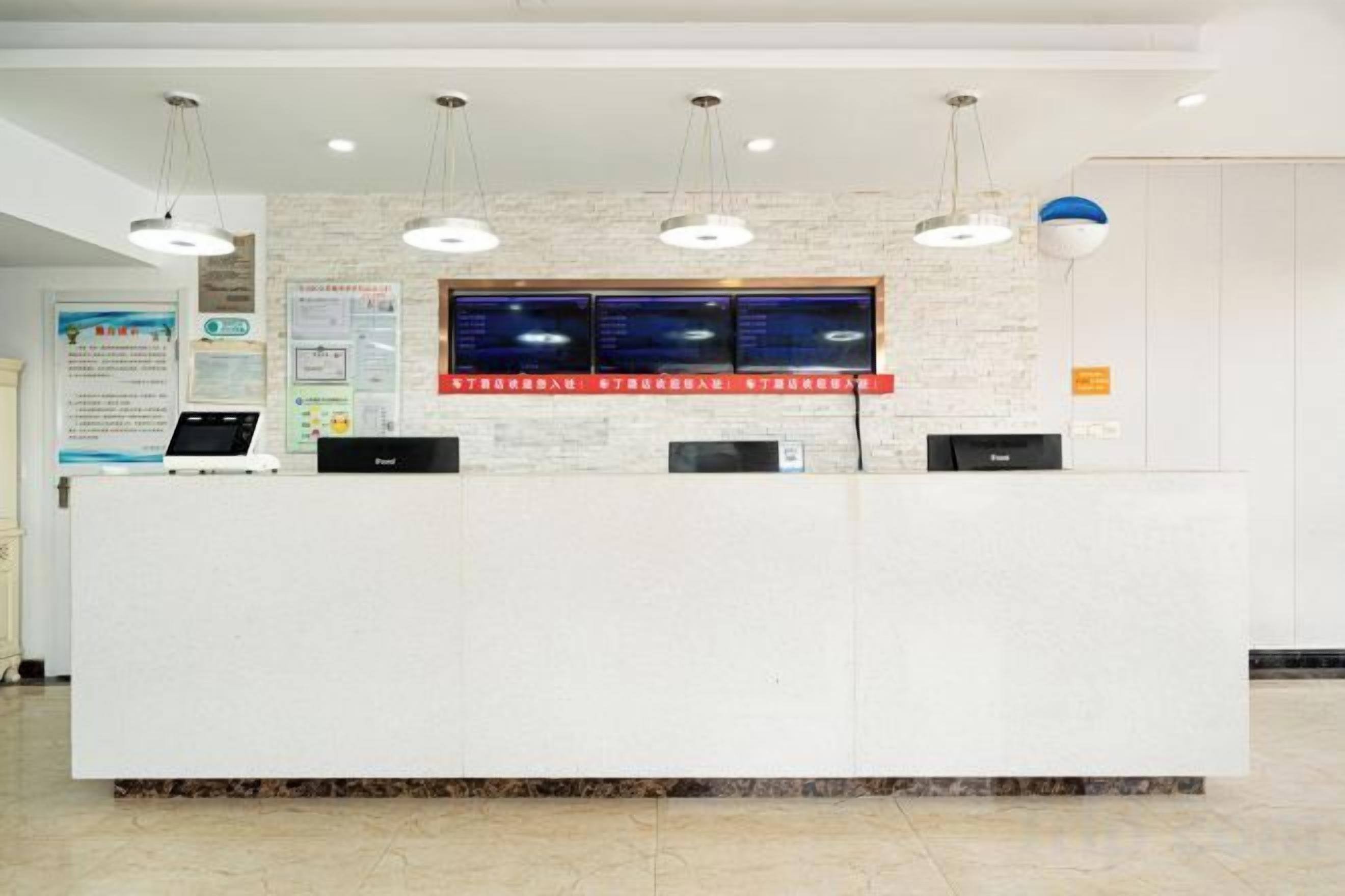 Un comptoir d’accueil équipé d’un ordinateur, d’un écran numérique et d’un panneau d’affichage fixé au mur.